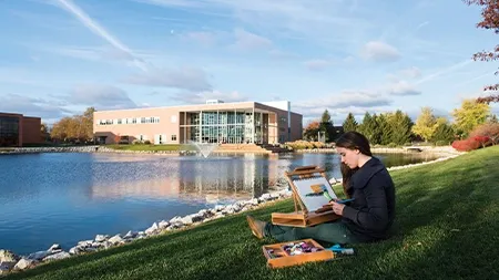 一个大学生坐在雪松湖畔的草地上画风景
