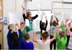 education major in classroom with young students with hands raised and papers in hand