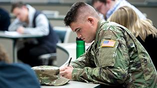 Man in army uniform taking notes in class.